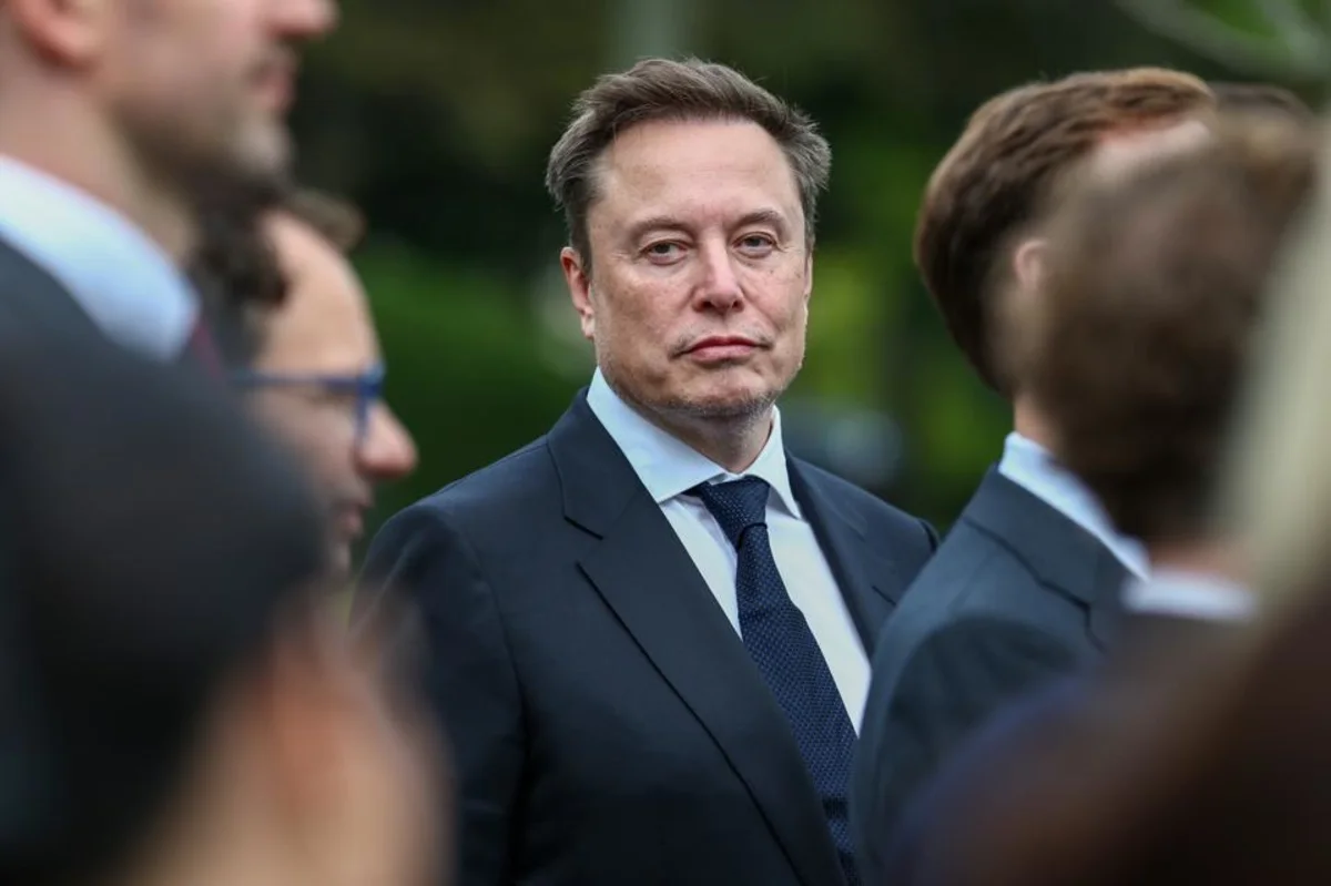 Elon Musk tersenyum dalam sebuah acara dengan latar belakang logo perusahaan teknologi miliknya