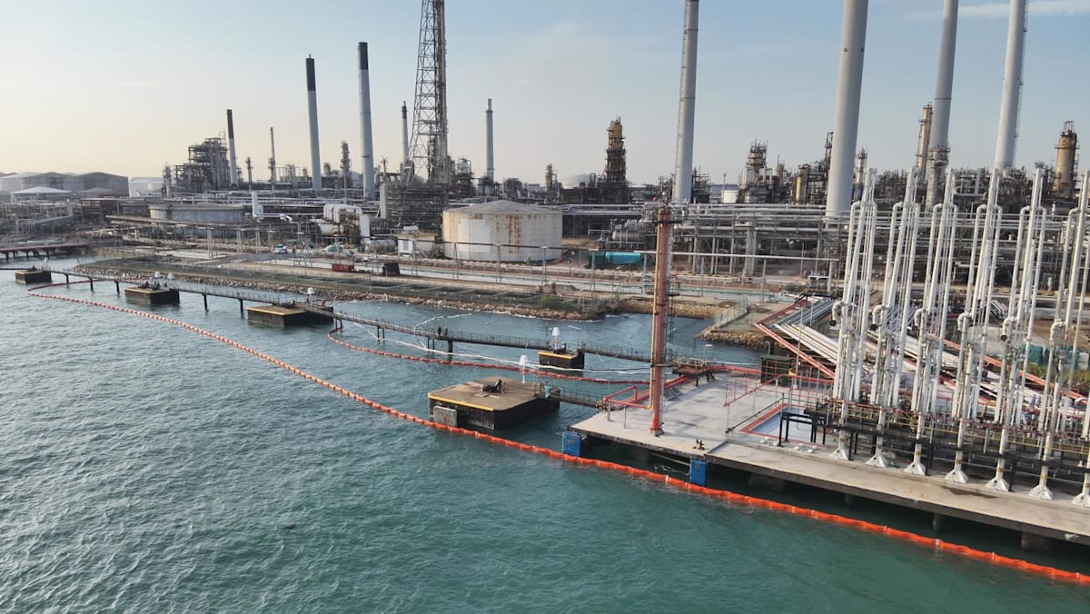 Pekerja dan petugas memasang pembatas minyak di perairan Pulau Bukom setelah insiden kebocoran.